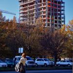 A woman awaits to cross Dawson Street as the Quorum Center peeks over the trees. 