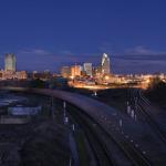 The last car of a long train sweeps past downtown Raleigh.