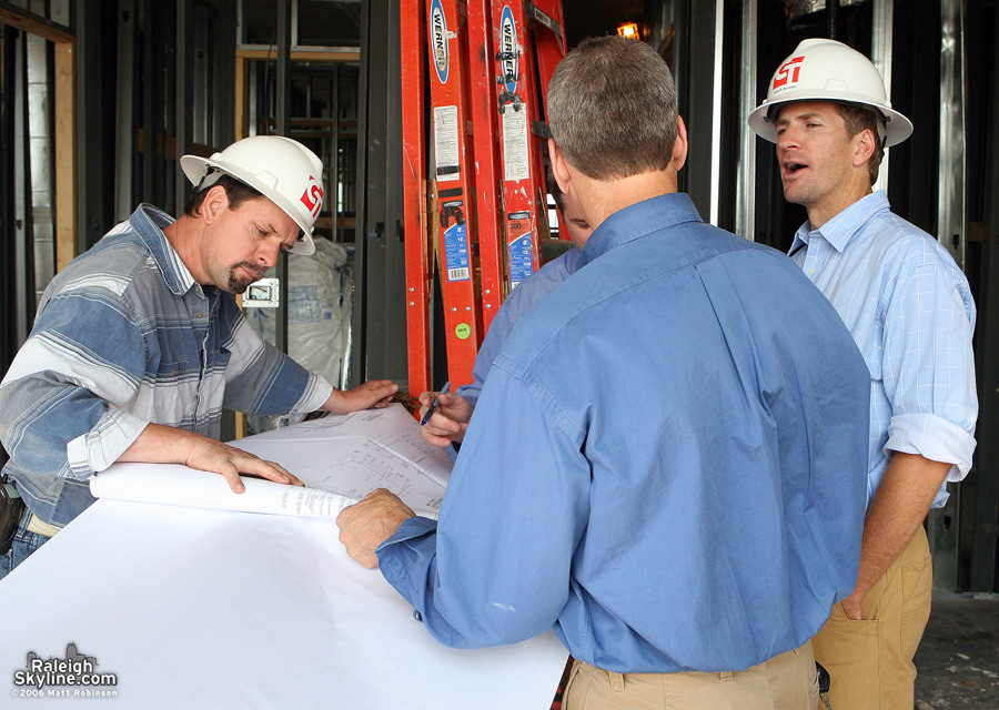 David Reynolds and unidentified men chat while looking at building plans for the Quorum Center.