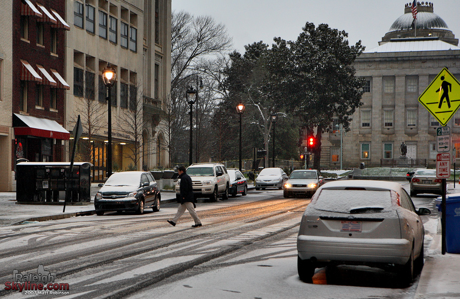 Snow rests on the North Carolina State Capitol dome as a man crosses the street.