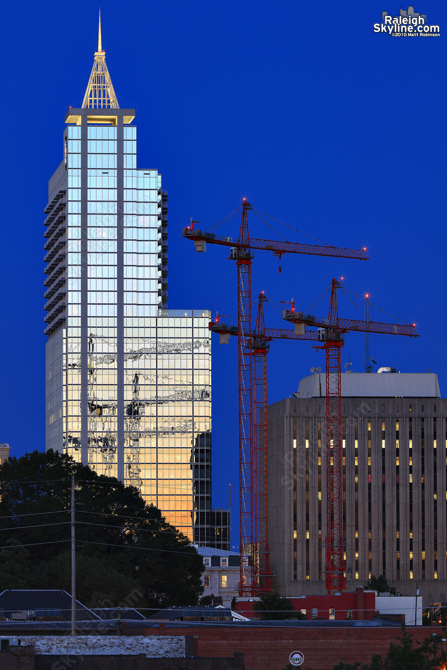 Three tower cranes for the new Wake County Courthouse reflect in RBC Plaza