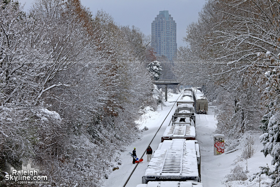 Snowy Norfolk Southern train passes snowboarders in Raleigh