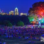 Downtown Raleigh looms over the crowds gathered to see the "Light the Woods with Sound" installation at Dorothea Dix Park