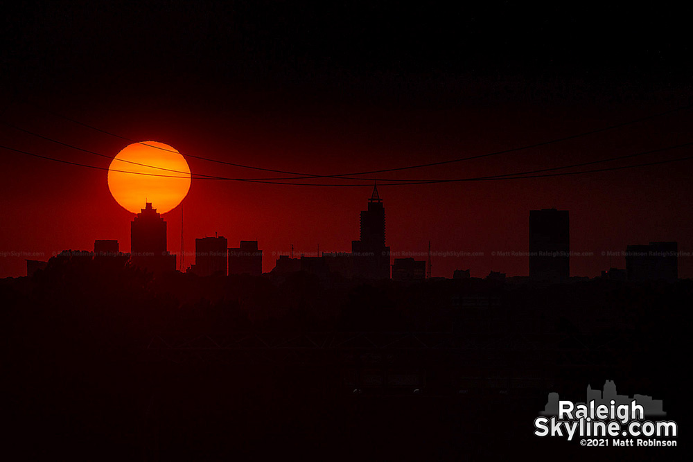 The sun setting behind the Raleigh cityscape from long range.